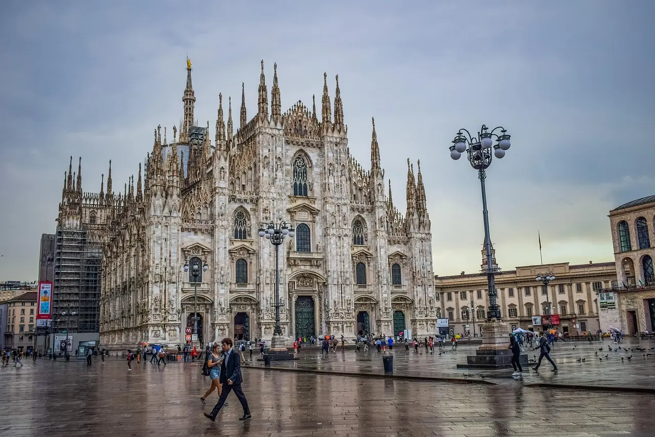 Catedral del Duomo de Milán con andamios y gente caminando por la plaza mojada bajo un cielo nublado