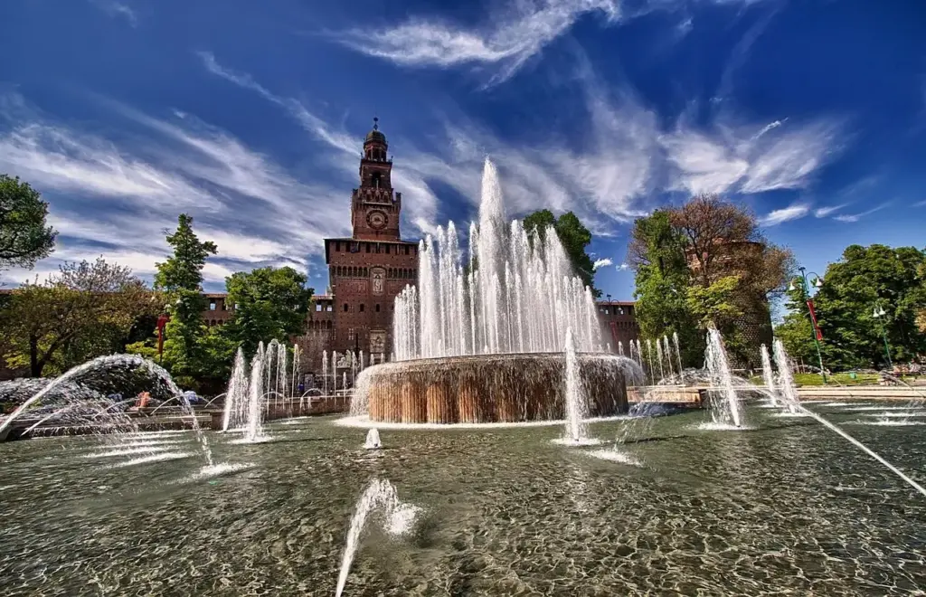 Fuente con chorros de agua frente a la torre del reloj del Castello Sforzesco de Milán